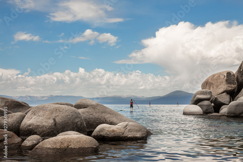 Paddleboarders paddling behind giant bounders of Sand Harbor in Lake Tahoe with mountains in the distance photo