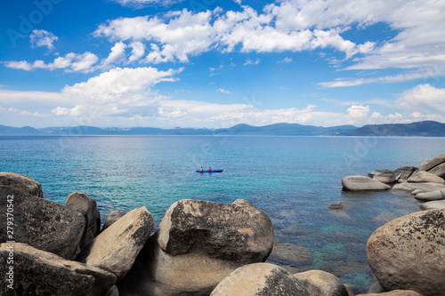 Tandem kayak in the middle of beautiful blue water of Lake Tahoe with boulders in the foreground