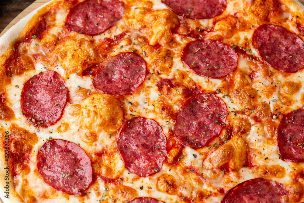 Delicious hot homemade Pepperoni pizza on the wooden table. Pepperoni Pizza - Fresh homemade pizza with pepperoni, cheese and tomato sauce on rustic black stone background with copy space.