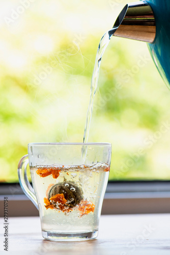 Flowering tea. Brewed Chinese teabloom in a transparent glass mug opposite the open window with a spring or summer view. photo