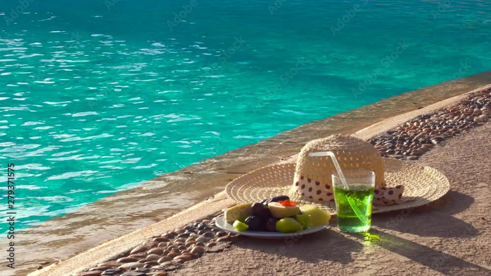 Plate with exotic fruits and drink left by swimming pool. Summer vacation. All inclusive