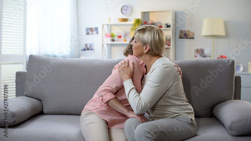 Unhappy mature female and daughter hugging on sofa, loss breakup and support