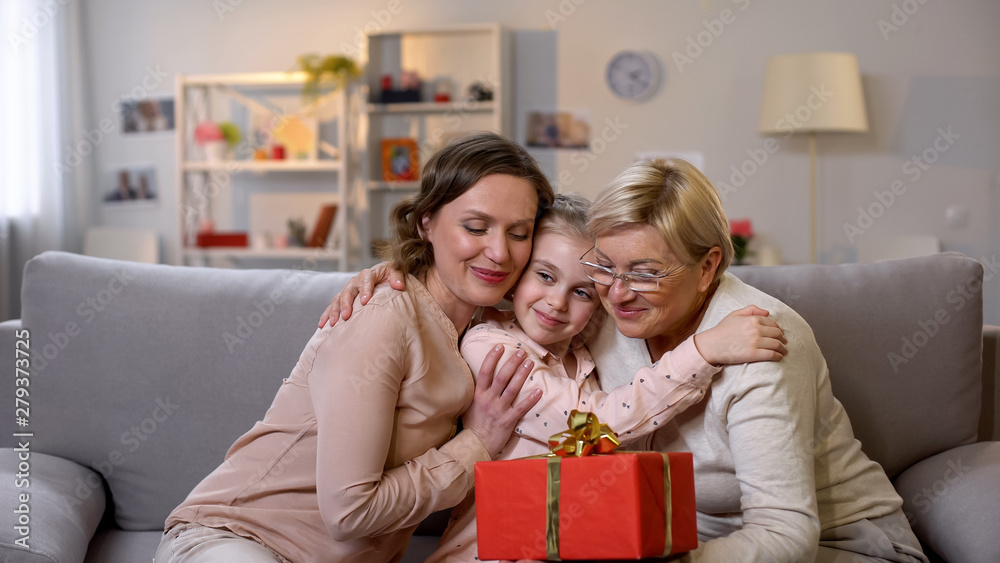 Multi-generation females hugging, granny holding gift box, attention and care Multi-generation females hugging, granny holding gift box, attention and care