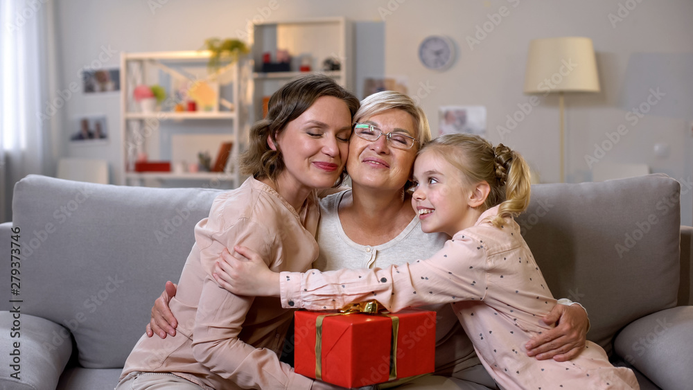 Females hugging granny holding gift box, present from daughter and granddaughter Females hugging granny holding gift box, present from daughter and granddaughter