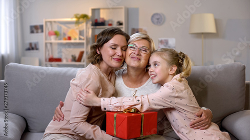 Females hugging granny holding gift box, present from daughter and granddaughter