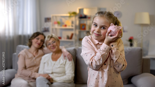 Photography Daughter holding piggybank, mother and granny behind, teaching to save money