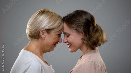 Adult daughter and mother touching foreheads looking each other, family love