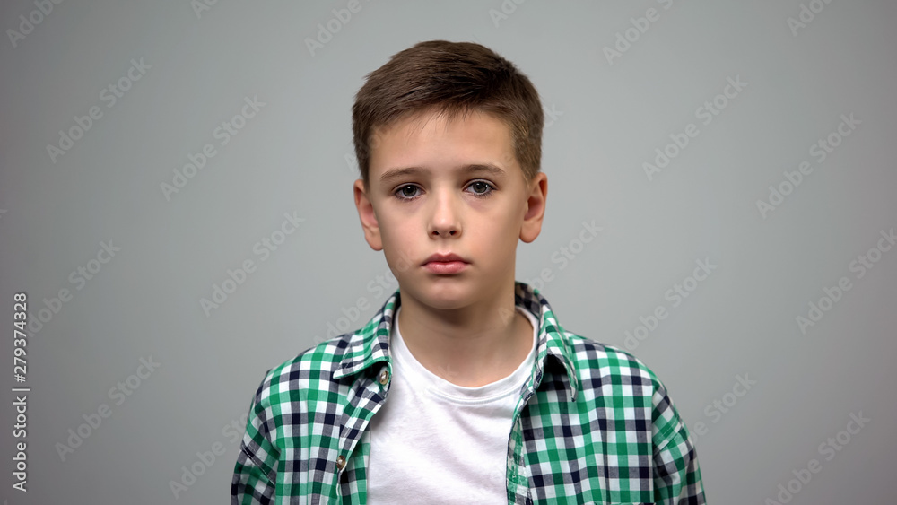 Scared male kid standing grey background, frightened child, orphanage bullying