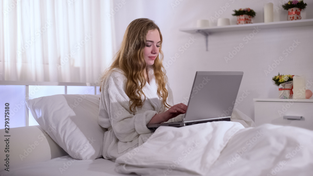 Freelancer in bathrobe working in bed on laptop, distant work for students Freelancer in bathrobe working in bed on laptop, distant work for students