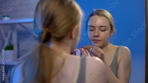 Female college student popping face pimples in front of mirror  dermatology