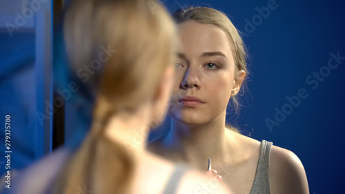 Young woman holding tweezers for eyebrow plucking and looking in mirror  beauty