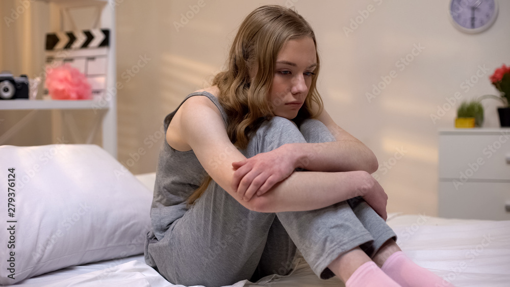 © motortion - Pensive teen girl sitting alone in bedroom feeling abandoned, puberty depression