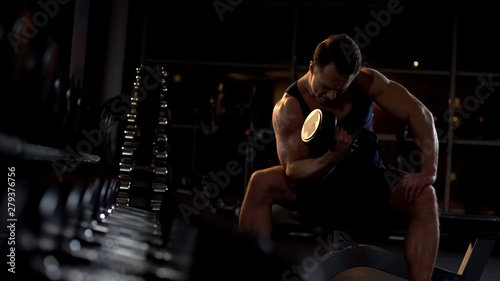 Photographie Motivated bodybuilder doing seated isolated dumbbell curl, evening workout