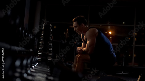 Strong bodybuilder resting after intensive workout with dumbbells at the gym