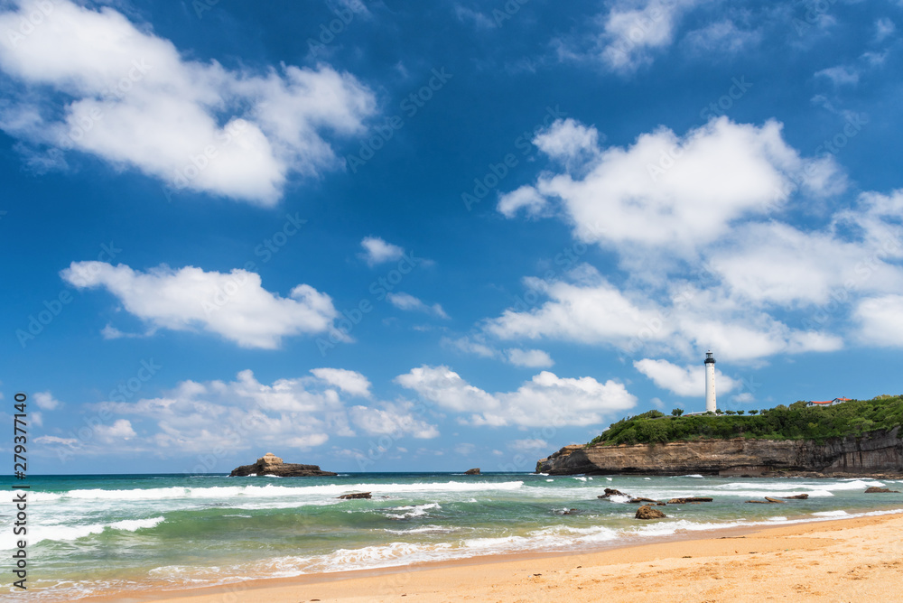 Naklejka premium Beach in Biarritz city with the lighthouse and white clouds on a polarised blue sky. Basque coast of France.