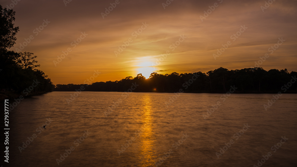 Golden sunset over the lake with smooth water in the foreground and smooth cloud in the background 