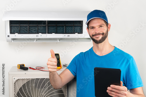 Installation service fix  repair maintenance of an air conditioner indoor unit, by cryogenist technican worker giving thumbs up ready to go after commissioning in blue shirt  baseball cap photo