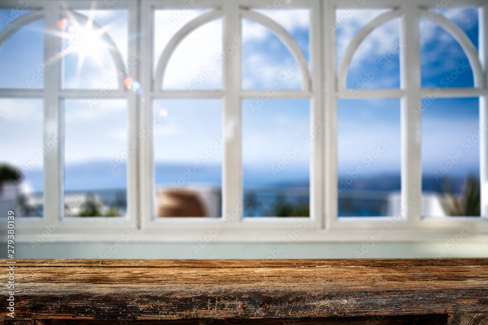 Fototapeta premium Table background with wooden top board and white window. Beautiful blurred ocean and beach view outside the window.
