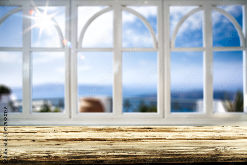 Fototapeta premium Table background with wooden top board and white window. Beautiful blurred ocean and beach view outside the window.