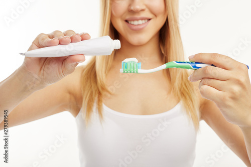 Blonde girl smiles while using toothpaste and toothbrush.