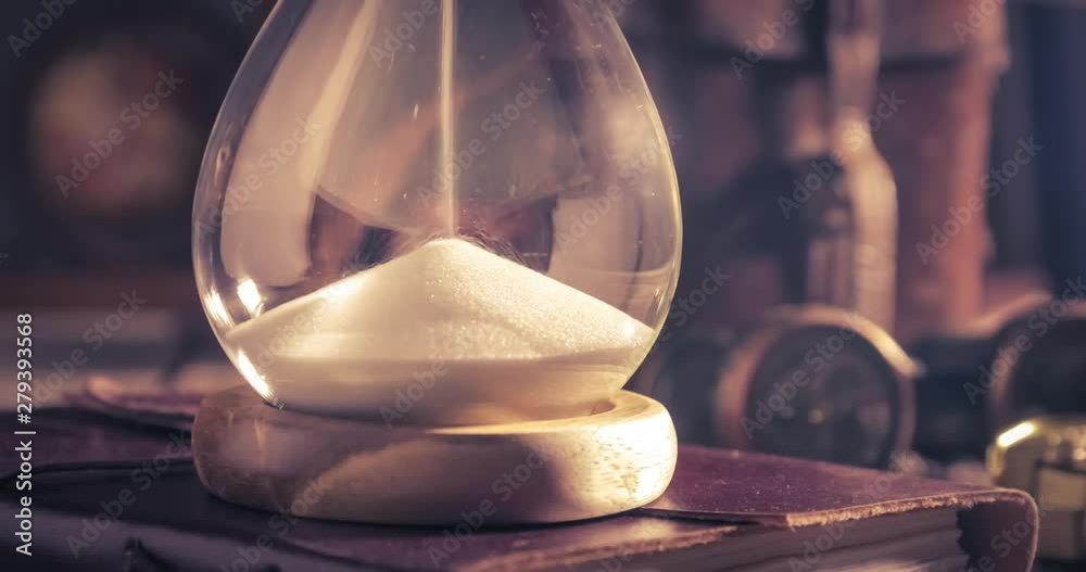 Flowing sand in an hourglass standing on a retro journey diary