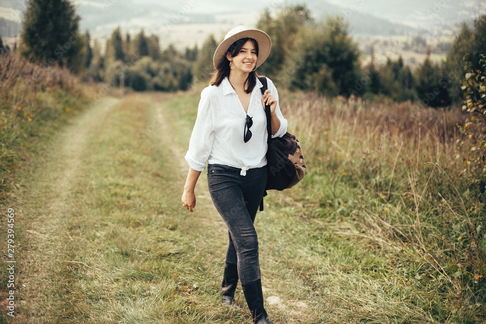 Happy hipster girl with backpack traveling on top of sunny mountain, walking on hills with woods. Stylish woman smiling and enjoying hiking in mountains. Wanderlust and travel. Happy hipster girl with backpack traveling on top of sunny mountain, walking on hills with woods. Stylish woman smiling and enjoying hiking in mountains. Wanderlust and travel.
