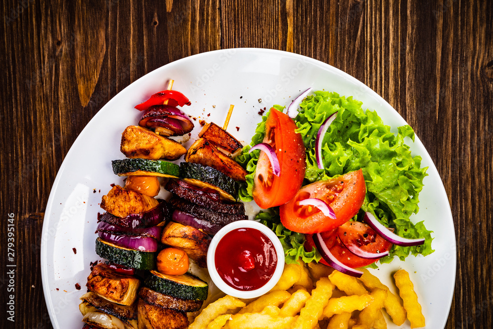 Kebabs - grilled meat with french fries and vegetables on wooden background Kebabs - grilled meat with french fries and vegetables on wooden background
