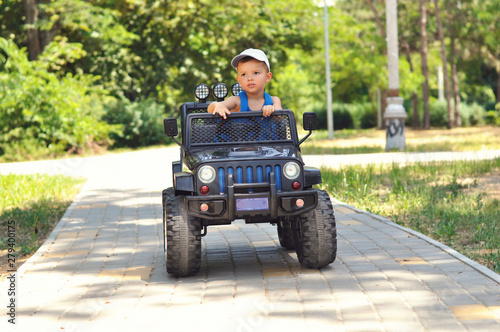 A cute, little boy drives an electric black car in a summer park. © volkonskaya