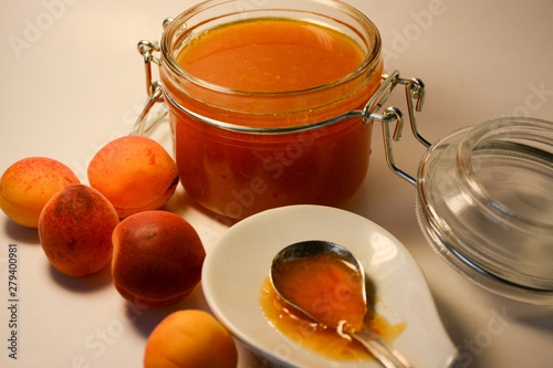 Jam in a glass jar, spoon in a plate and apricots in a glass jar