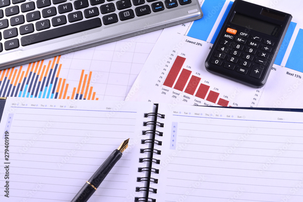 Blank Notebook with calculator, keyboard and fountain pen on graphs, charts and business table. The workplace of business people Blank Notebook with calculator, keyboard and fountain pen on graphs, charts and business table. The workplace of business people