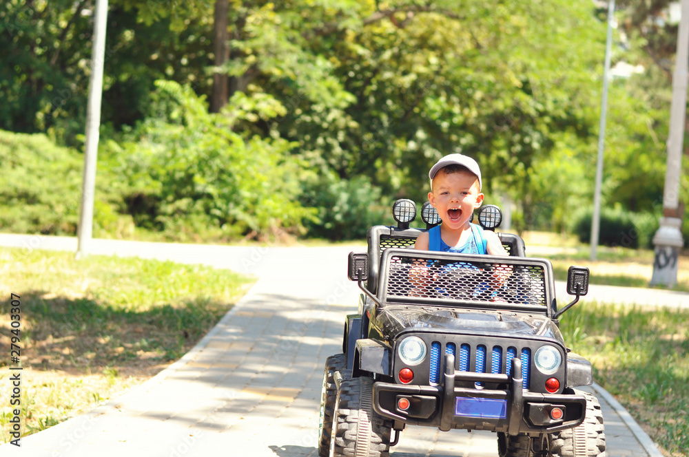 A cute, little boy drives an electric black car in a summer park.	