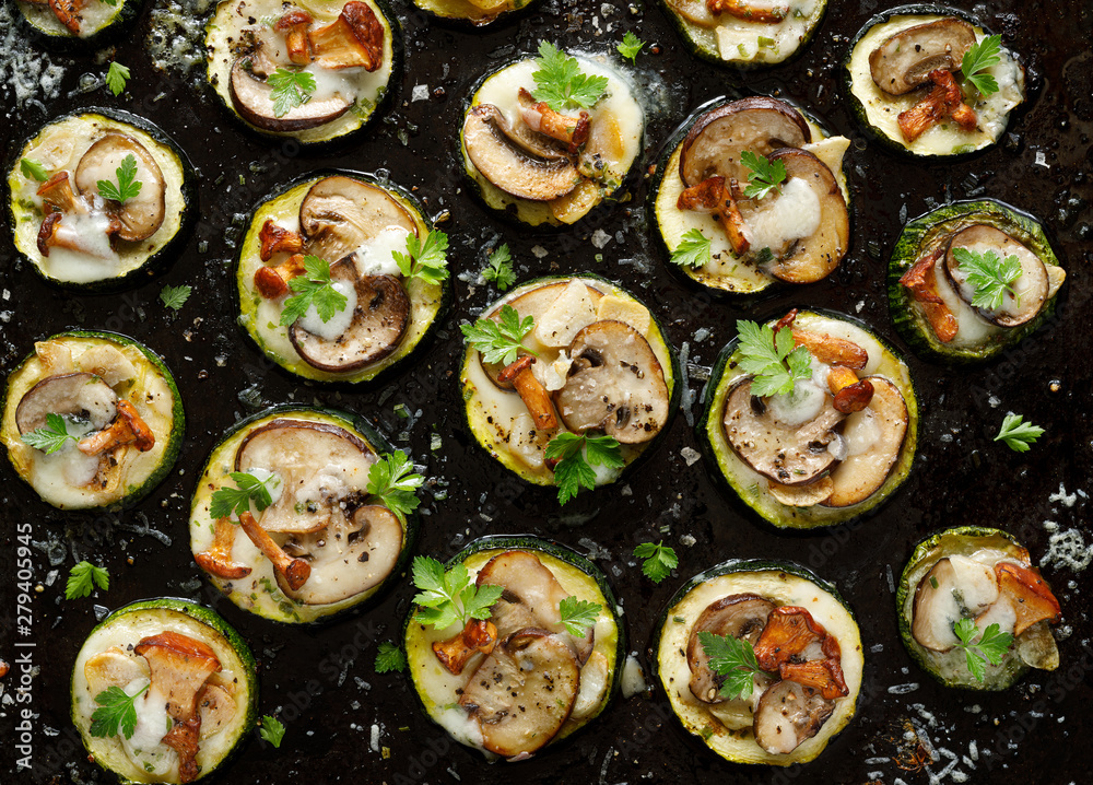 Mini pizzas from zucchini slices with the addition of brown mushrooms, mushroom chanterelles, mozzarella cheese and herbs on a black background, top view. Vegetarian food Mini pizzas from zucchini slices with the addition of brown mushrooms, mushroom chanterelles, mozzarella cheese and herbs on a black background, top view. Vegetarian food