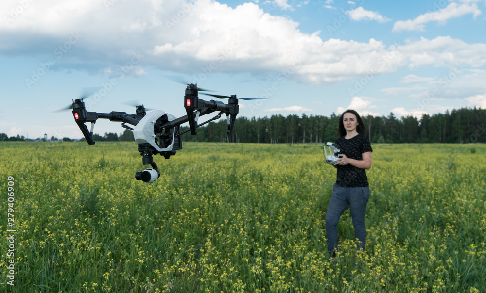 The girl controls the quadcopter. Drone in flight over the field. The operator of the drone. Forest, sky and clouds. The girl controls the quadcopter. Drone in flight over the field. The operator of the drone. Forest, sky and clouds.