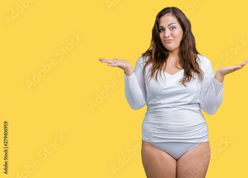 Beautiful plus size young overwight woman wearing white underwear over isolated background clueless and confused expression with arms and hands raised. Doubt concept. © Krakenimages.com