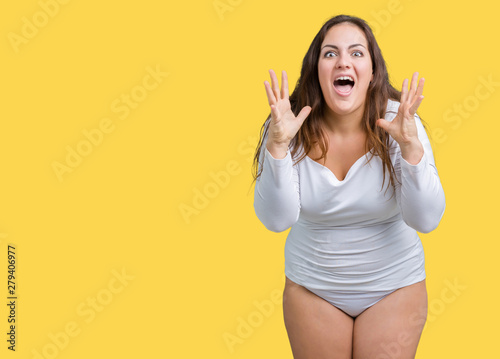Beautiful plus size young overwight woman wearing white underwear over isolated background celebrating crazy and amazed for success with arms raised and open eyes screaming excited. Winner concept