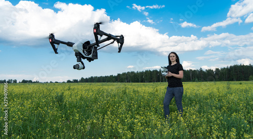 The girl controls the quadcopter. Drone in flight over the field. The operator of the drone. Forest  sky and clouds.