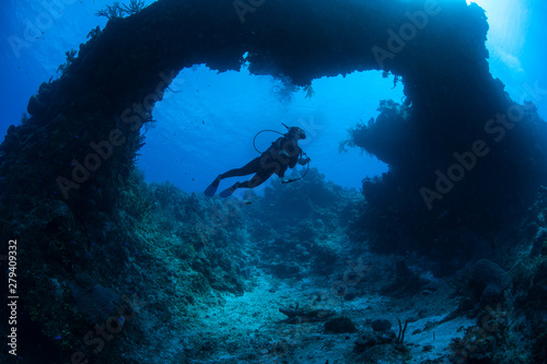 A scuba diver explores a submerged natural arch formed on a coral reef off the coast of Grand Cayman in the Caribbean Sea. This beautiful area is a popular destination for divers and snorkelers. © ead72