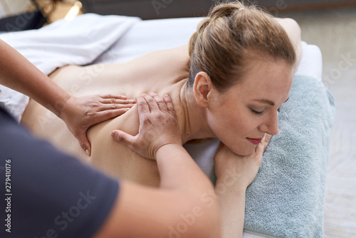 Chinese woman massage therapist giving a treatment to an attractive blond client on massage table in a bright medical office