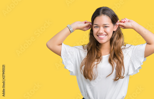 Young beautiful brunette business woman over isolated background Smiling pulling ears with fingers, funny gesture. Audition problem