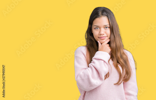 Young beautiful brunette woman wearing pink winter sweater over isolated background looking confident at the camera with smile with crossed arms and hand raised on chin. Thinking positive.