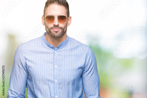 Young handsome man wearing sunglasses over isolated background with serious expression on face. Simple and natural looking at the camera.