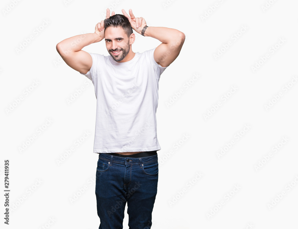 Fototapeta premium Handsome man wearing white t-shirt over white isolated background Posing funny and crazy with fingers on head as bunny ears, smiling cheerful
