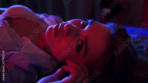 A girl in seductive underwear lies on a bed, poses and looks sexually straight to the camera. Romantic mood, seduction, attraction. Date, confidence. Female portrait, close up view