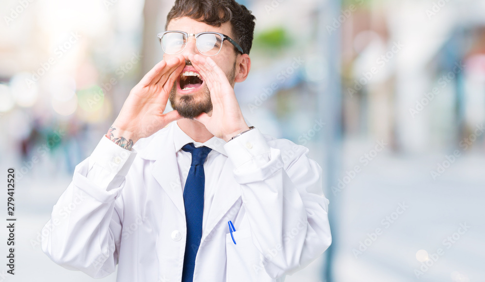 Young professional scientist man wearing white coat over isolated background Shouting angry out loud with hands over mouth Young professional scientist man wearing white coat over isolated background Shouting angry out loud with hands over mouth