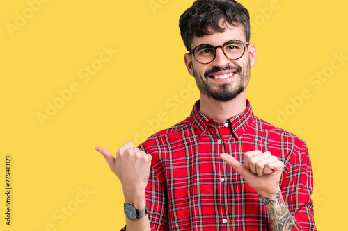 Young handsome man wearing glasses over isolated background Pointing to the back behind with hand and thumbs up, smiling confident photo