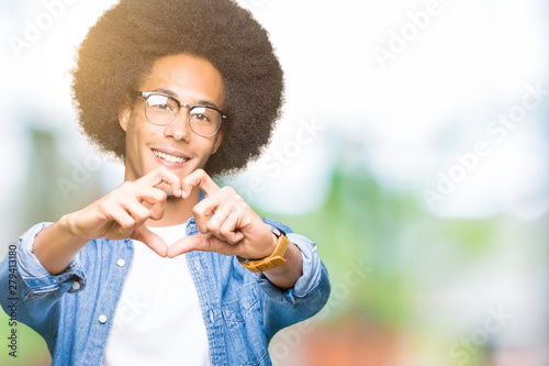 Young african american man with afro hair wearing glasses smiling in love showing heart symbol and shape with hands. Romantic concept.