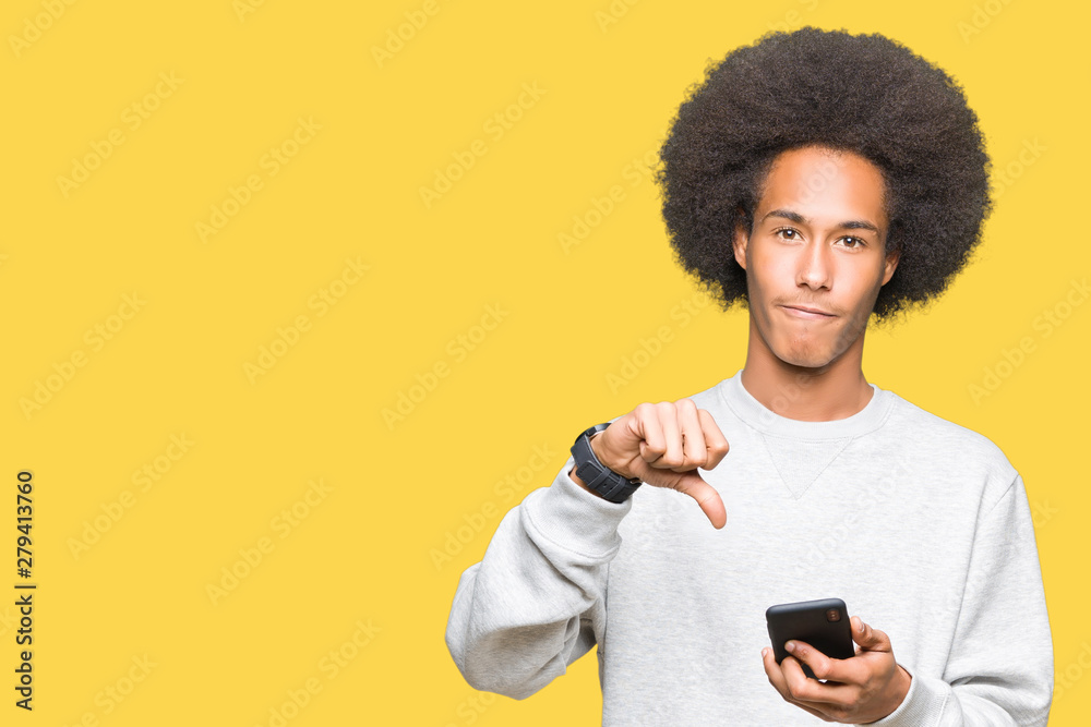 Young african american man with afro hair using a smartphone with angry face, negative sign showing dislike with thumbs down, rejection concept Young african american man with afro hair using a smartphone with angry face, negative sign showing dislike with thumbs down, rejection concept