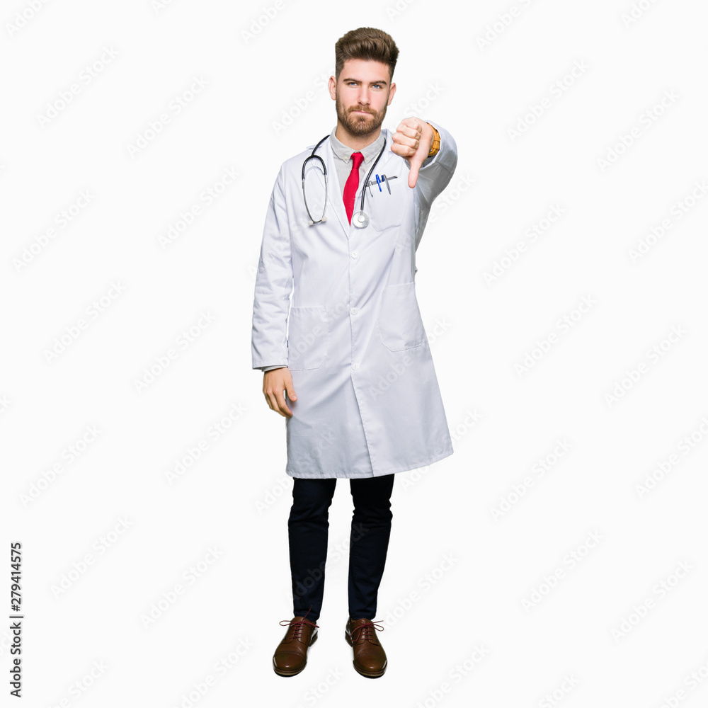 Young handsome doctor man wearing medical coat looking unhappy and angry showing rejection and negative with thumbs down gesture. Bad expression. Young handsome doctor man wearing medical coat looking unhappy and angry showing rejection and negative with thumbs down gesture. Bad expression.