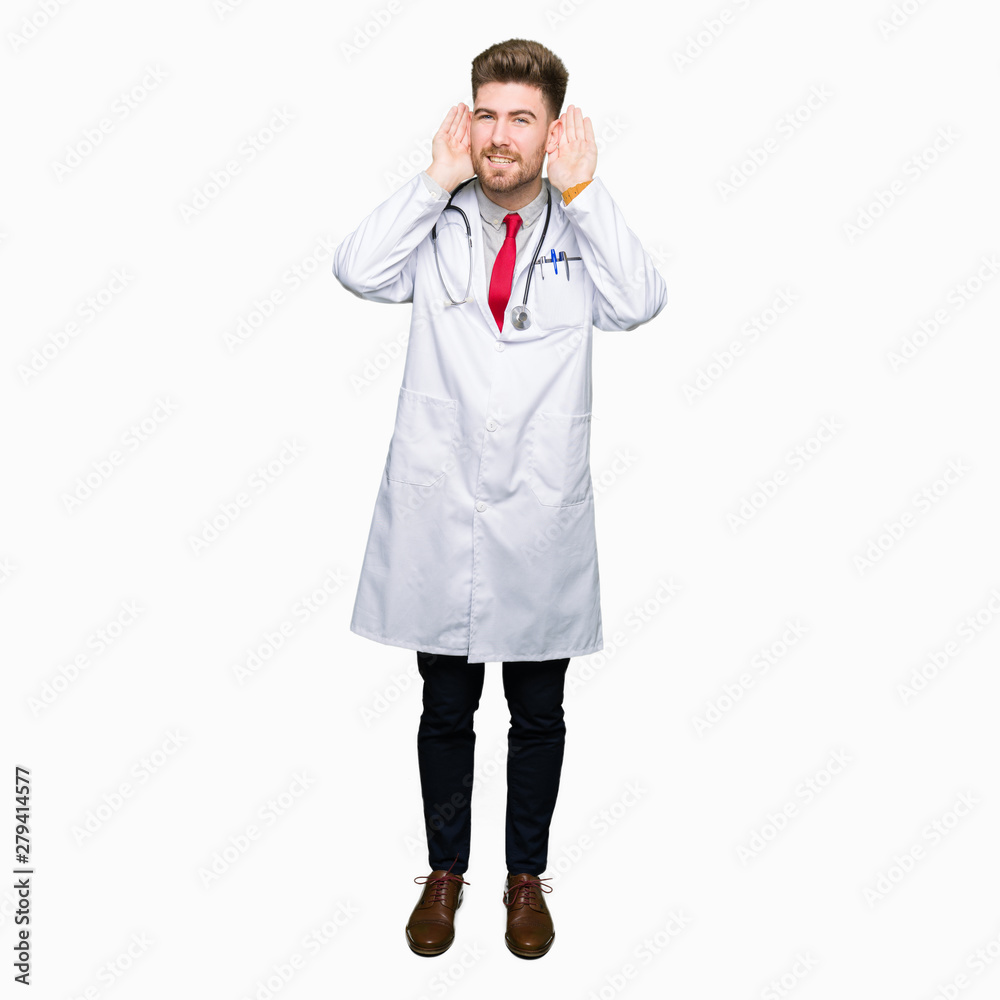Young handsome doctor man wearing medical coat Trying to hear both hands on ear gesture, curious for gossip. Hearing problem, deaf Young handsome doctor man wearing medical coat Trying to hear both hands on ear gesture, curious for gossip. Hearing problem, deaf