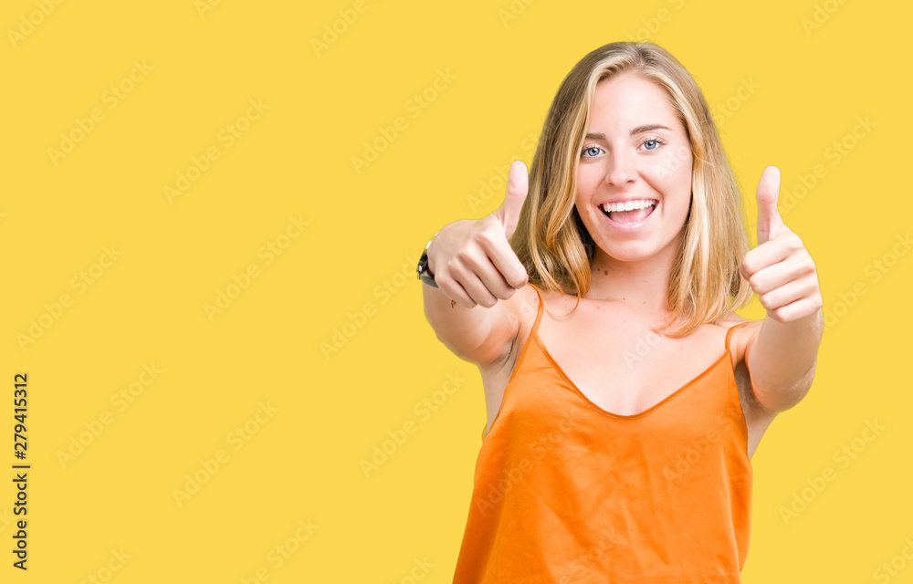 Beautiful young woman wearing orange shirt over isolated background approving doing positive gesture with hand, thumbs up smiling and happy for success. Looking at the camera, winner gesture. Beautiful young woman wearing orange shirt over isolated background approving doing positive gesture with hand, thumbs up smiling and happy for success. Looking at the camera, winner gesture.